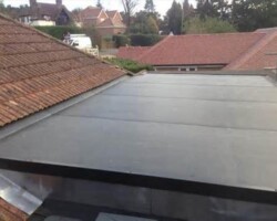 Grey GRP flat roof surrounded by tiled roofs and garden in Gloucestershire