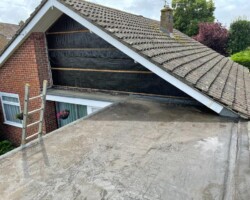 Repaired grey flat roof beside a brick gable on a Gloucestershire home